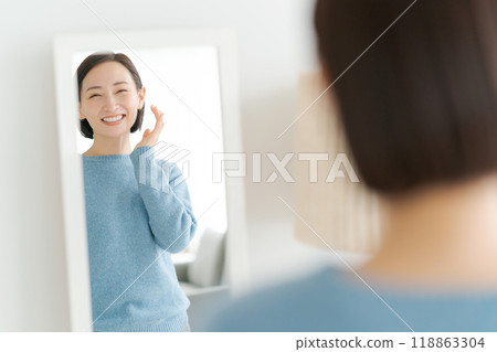 A woman looking at a mirror and smiling A woman looking at a mirror and smiling 118863304