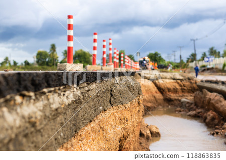 An asphalt road is severely damaged by erosion and flooding, clearly exposing the layers of rock and soil beneath. The scene highlights the impact of natural forces on infrastructure. An asphalt road is severely damaged by erosion and flooding, clearly exposing the layers of rock and soil beneath. The scene highlights the impact of natural forces on infrastructure. 118863835