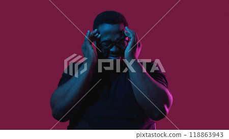 Headache pain. Stress problem. Anxiety trouble. Upset depressed man suffering from migraine ache in neon light isolated on burgundy background. Headache pain. Stress problem. Anxiety trouble. Upset depressed man suffering from migraine ache in neon light isolated on burgundy background. 118863943