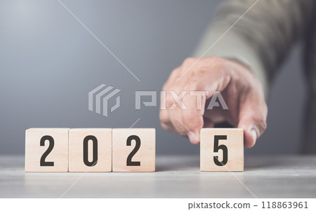 Hand replaces "2024" with "2025" using number blocks, symbolizing the transition into the new year, representing change, progress, and the ongoing passage of time Hand replaces "2024" with "2025" using number blocks, symbolizing the transition into the new year, representing change, progress, and the ongoing passage of time 118863961