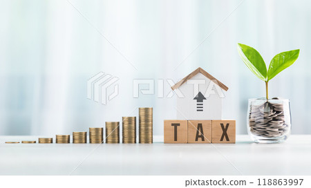 TAX is write on a wooden block next to a stack of coins and a house model and coins jar with small plant on a wooden table. Tax awareness, financial planning, savings, and effective money management 118863997