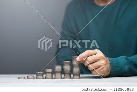 Man is stacking coins on a table, arranging them from smallest to largest. The image represents financial growth, savings, and careful money management 118863998