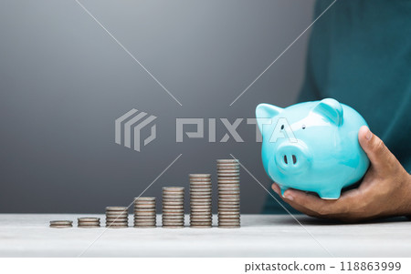Man is dropping coins into a blue piggy bank, symbolizing the act of saving and financial responsibility. Financial planning, budgeting, and building a stable future through consistent savings 118863999