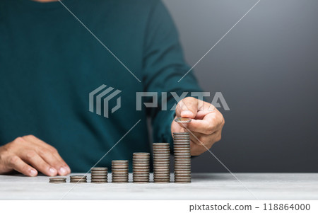 Man is stacking coins on a table, arranging them from smallest to largest. The image represents financial growth, savings, and careful money management 118864000