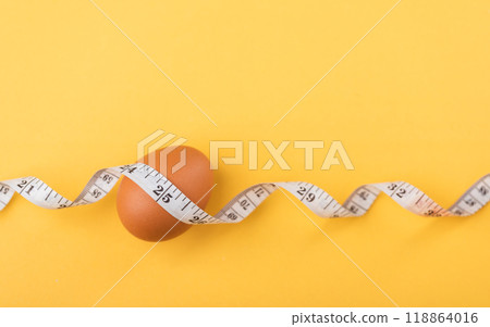Fresh egg and measuring tape on a table symbolize the idea of eating eggs for weight loss or health. The image highlights eggs as a nutritious choice for a balanced diet and fitness goals Fresh egg and measuring tape on a table symbolize the idea of eating eggs for weight loss or health. The image highlights eggs as a nutritious choice for a balanced diet and fitness goals 118864016