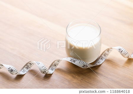 Glass of milk and a measuring tape on the table. Concept of incorporating milk into a healthy diet and fitness plan, highlighting its nutritional benefits for weight management and overall health 118864018