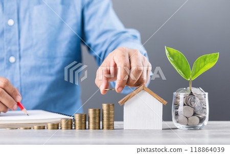 Businessman stacks coins, symbolizing saving and financial growth. A jar of coins with a seedling in the center and a wooden house model sit on the table, with coins arranged from smallest to largest Businessman stacks coins, symbolizing saving and financial growth. A jar of coins with a seedling in the center and a wooden house model sit on the table, with coins arranged from smallest to largest 118864039