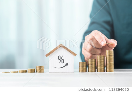 Man is stacking coins on a table, arranging them from smallest to largest, with a wooden house model beside him. Emphasizes the concept of saving money for future investments and financial stability Man is stacking coins on a table, arranging them from smallest to largest, with a wooden house model beside him. Emphasizes the concept of saving money for future investments and financial stability 118864050