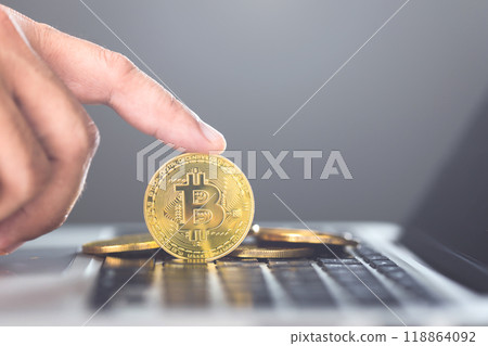 Man holds a golden Bitcoin while using a laptop, representing Bitcoin as a form of digital currency for online transactions, highlighting the concept of modern financial technology and crypto usage 118864092