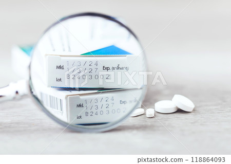 Close-up of the production code and expiration date printed on the side of a medicine box, with pills placed on a table. The image highlights the importance of checking medication before consumption 118864093