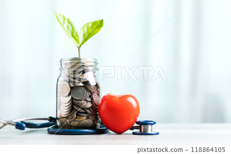 Savings concept for future healthcare. A jar filled with coins and a small plant in the center, accompanied by a heart and a stethoscope, symbolizing saving money for good health in the future 118864105