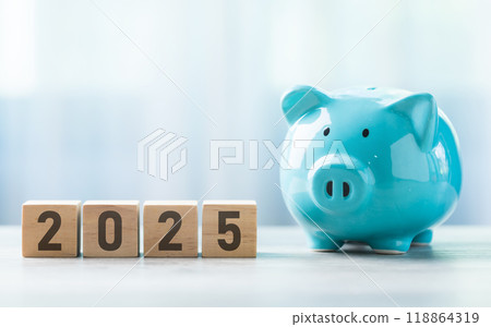 2025 is written on a wooden block beside a A blue piggy bank on a wooden table against a bright white background. Money planning and Financial planning, savings, and wise money management. 2025 is written on a wooden block beside a A blue piggy bank on a wooden table against a bright white background. Money planning and Financial planning, savings, and wise money management. 118864319