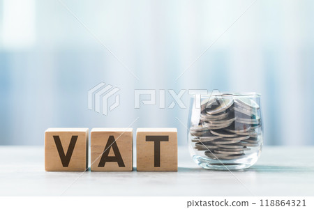 VAT is written on a wooden block beside a clear glass coins jar on a wooden table against a bright white background. Tax and Financial planning, savings, and wise money management. 118864321