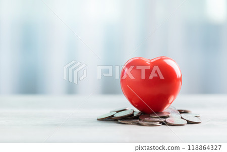 Red heart and a pile of coins on a table against a bright white background. The image symbolizes saving money for health care or financial well-being. Red heart and a pile of coins on a table against a bright white background. The image symbolizes saving money for health care or financial well-being. 118864327