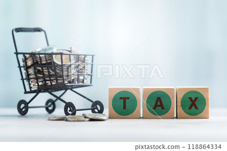 TAX is written on a wooden block and coins in a shopping cart on a wooden table against a bright white background. Commercial tax and Financial planning, savings, and wise money management. 118864334