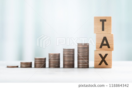 TAX is written on a wooden block beside a stack of coins on a wooden table against a bright white background. Tax and Financial planning, savings, and wise money management. TAX is written on a wooden block beside a stack of coins on a wooden table against a bright white background. Tax and Financial planning, savings, and wise money management. 118864342