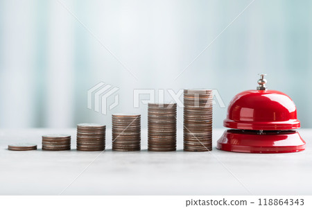 A close-up of a red service bell next to a coins stack on a wooden table against a bright white background. The image represents a call to action for financial planning and savings. A close-up of a red service bell next to a coins stack on a wooden table against a bright white background. The image represents a call to action for financial planning and savings. 118864343
