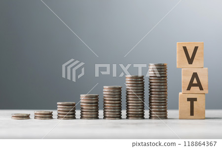 "VAT" is written on a wooden block, placed next to a pile of coins on a wooden table against a grey background. The image symbolizes tax, financial management, and budgeting "VAT" is written on a wooden block, placed next to a pile of coins on a wooden table against a grey background. The image symbolizes tax, financial management, and budgeting 118864367