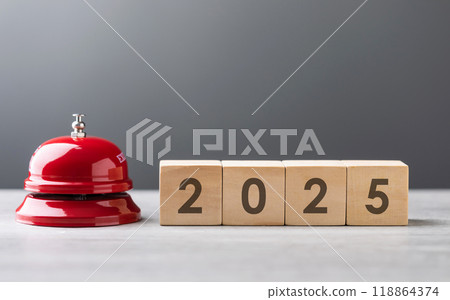 Red service bell and a wooden block displaying "2025" are placed side by side, symbolizing a call to action for the new year. The scene highlights themes of preparation, planning, and fresh beginnings Red service bell and a wooden block displaying "2025" are placed side by side, symbolizing a call to action for the new year. The scene highlights themes of preparation, planning, and fresh beginnings 118864374