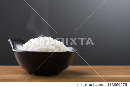 Cooked Thai jasmine rice served in a black bowl sits on a brown table against a dark grey backdrop. The studio shot highlights the fluffy texture and aromatic quality of the rice 118864376