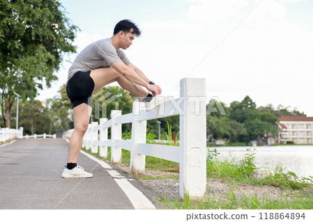 A sporty, fit Asian man in sportswear is tying his running shoelaces before running in the park. A sporty, fit Asian man in sportswear is tying his running shoelaces before running in the park. 118864894
