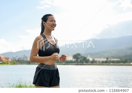 A sporty, fit Asian woman in sportswear is jogging or running in a public park on a bright day. A sporty, fit Asian woman in sportswear is jogging or running in a public park on a bright day. 118864907