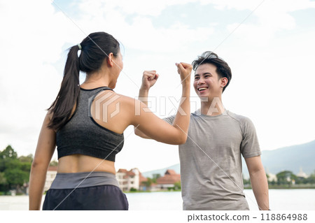 A cheerful, active Asian couple raises their fists in triumph after reaching their running target. 118864988