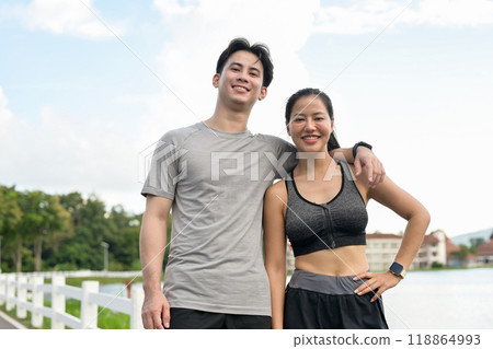A lovely, active Asian couple in sportswear stands in a park, smiling at the camera. A lovely, active Asian couple in sportswear stands in a park, smiling at the camera. 118864993