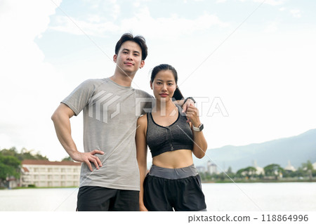 A lovely, active Asian couple in sportswear stands in a park, smiling at the camera. A lovely, active Asian couple in sportswear stands in a park, smiling at the camera. 118864996
