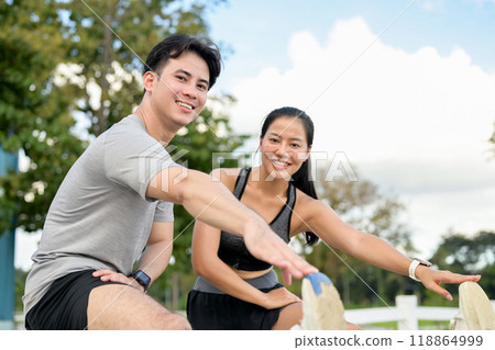 An active, sporty Asian couple smiles at the camera while stretching their legs before running. An active, sporty Asian couple smiles at the camera while stretching their legs before running. 118864999