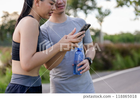 A couple in sportswear is looking at something on a smartphone together while resting after a run. A couple in sportswear is looking at something on a smartphone together while resting after a run. 118865018