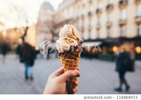 Hand holding an ice cream in a waffle cone, on the street of a beautiful city 118869415
