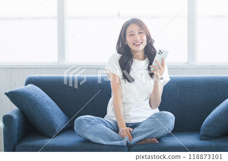 A young woman sitting on a sofa and relaxing with a smartphone 118873101