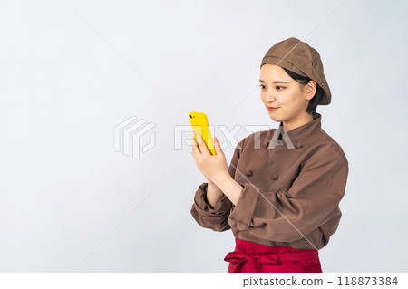 A woman in a cooking uniform using a smartphone, a chef, a restaurant employee A woman in a cooking uniform using a smartphone, a chef, a restaurant employee 118873384