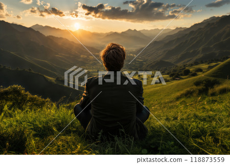 a man sits on the grass and looks at nature, a view of the hills and valley at sunset, a beautiful landscape, the concept of rest and relaxation 118873559