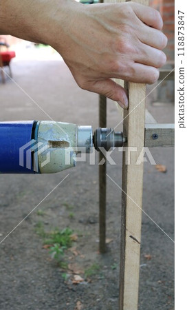 making a hole in the side of a poultry cage with a drill, drilling into a piece of wood in a structure of an outbuilding 118873847