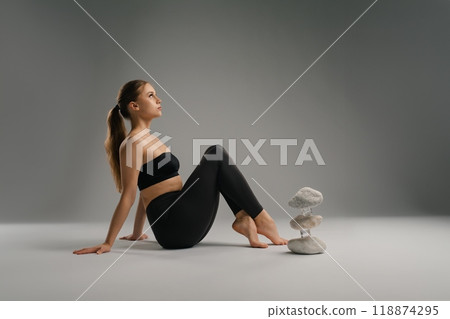 Woman practicing yoga with stone balancing art in a serene indoor setting 118874295