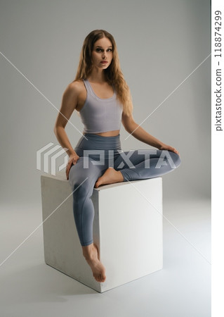 A young woman practices yoga poses on a cube in a minimalistic studio A young woman practices yoga poses on a cube in a minimalistic studio 118874299