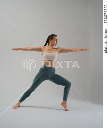 Woman performing yoga in warrior pose on a neutral background Woman performing yoga in warrior pose on a neutral background 118874301