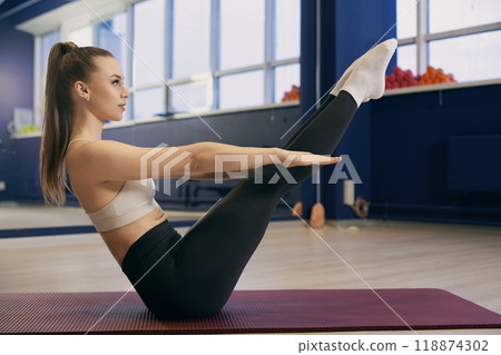 Woman practicing pilates on a mat in a bright fitness studio during daylight Woman practicing pilates on a mat in a bright fitness studio during daylight 118874302