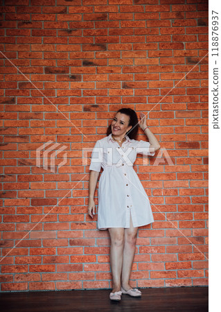 Brunette woman in dress smiling at brick wall 118876937