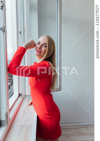 Beautiful blonde woman smiling at the window in the interior of a white room 118877077