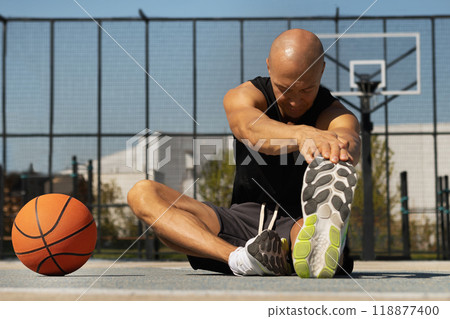 Basketball player stretching legs after game. Outdoors summer training. Healthy and sport lifestyle concept. 118877400