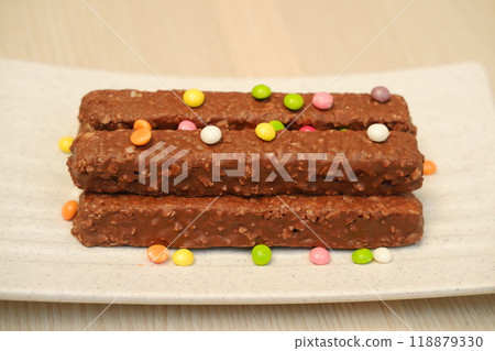 Chocolate bars on a white plate with colorful candies in the background Chocolate bars on a white plate with colorful candies in the background 118879330