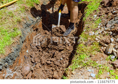 Worker digs trench for drainage pipe with shovel 118879775