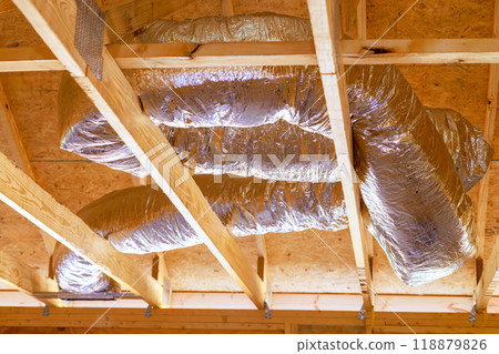 Installing ventilation HVAC pipes with silver insulation on roof ceiling during construction Installing ventilation HVAC pipes with silver insulation on roof ceiling during construction 118879826