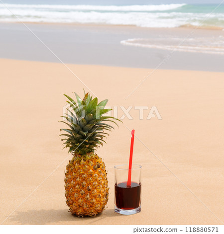 Ripe pineapple and juice in a glass on a sandy beach. Ripe pineapple and juice in a glass on a sandy beach. 118880571