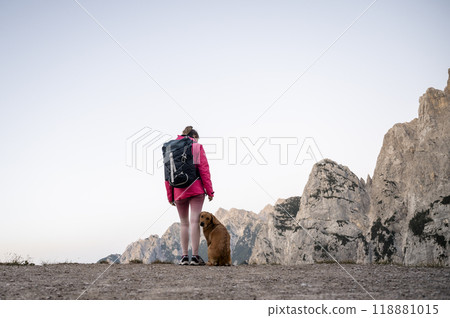 Female hiker in pink jacket standing on top of a mountain with her dog Female hiker in pink jacket standing on top of a mountain with her dog 118881015