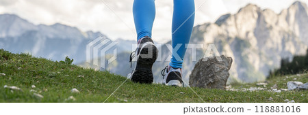 Low angle view of female legs in hiking shoes walking on a green mountain trail Low angle view of female legs in hiking shoes walking on a green mountain trail 118881016