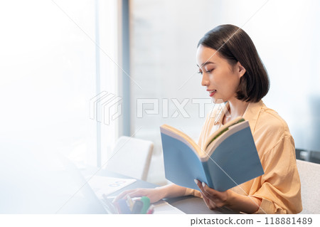 一位女士在電腦上工作，手裡拿著一本參考書 118881489